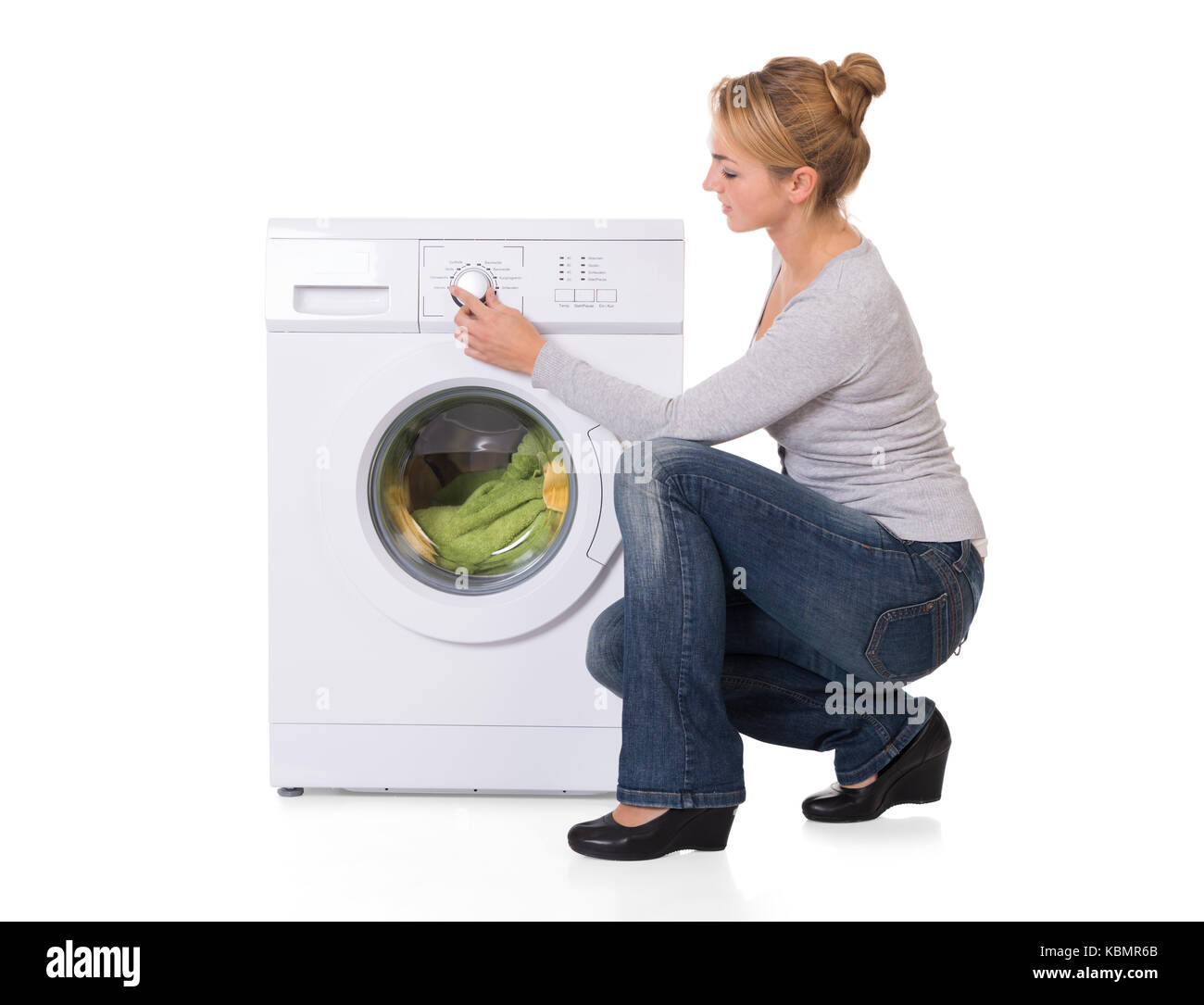Full length side view of young woman crouching while using washing machine over white background Stock Photo