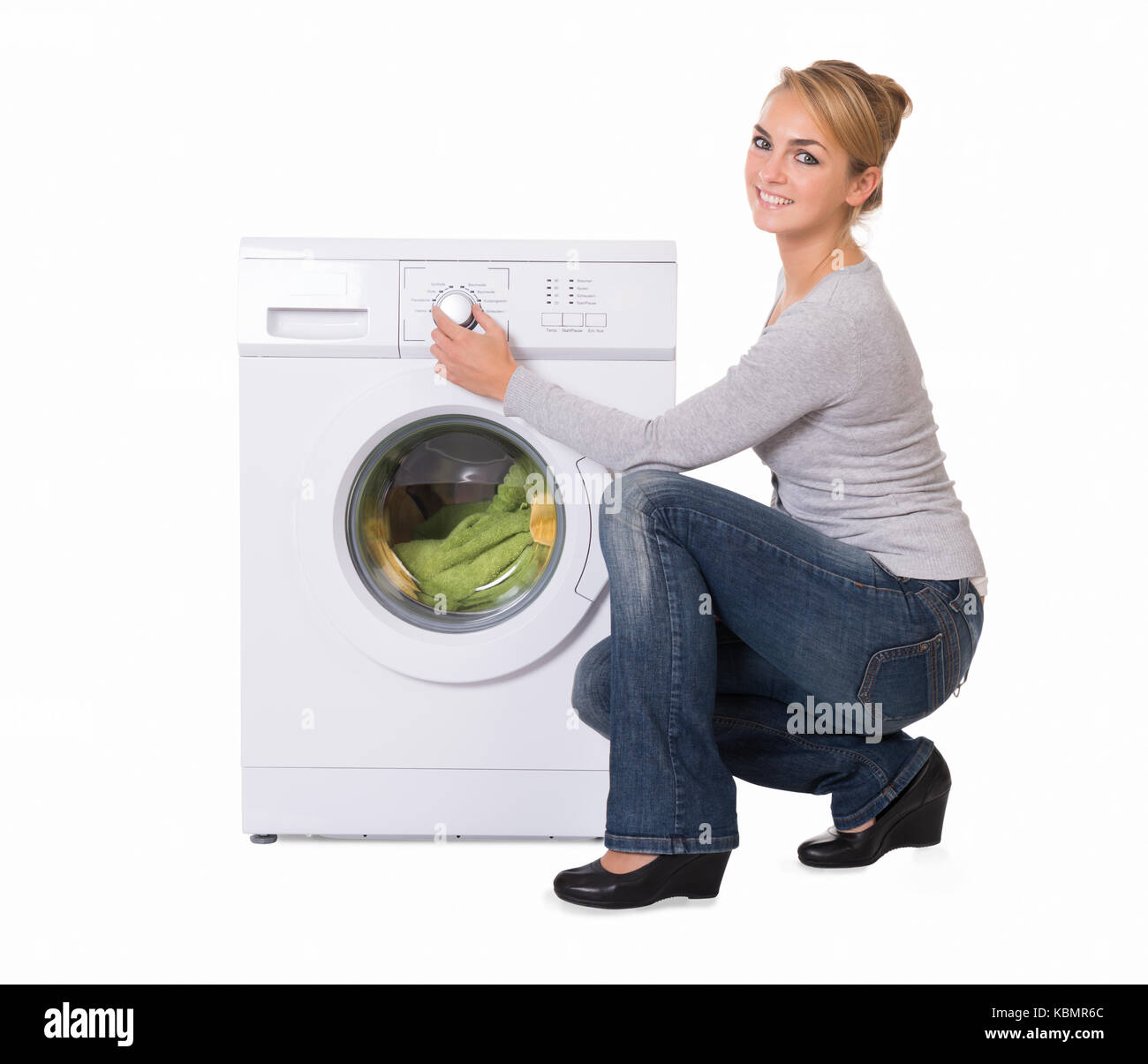 Full length side view of young woman crouching while using washing machine over white background Stock Photo