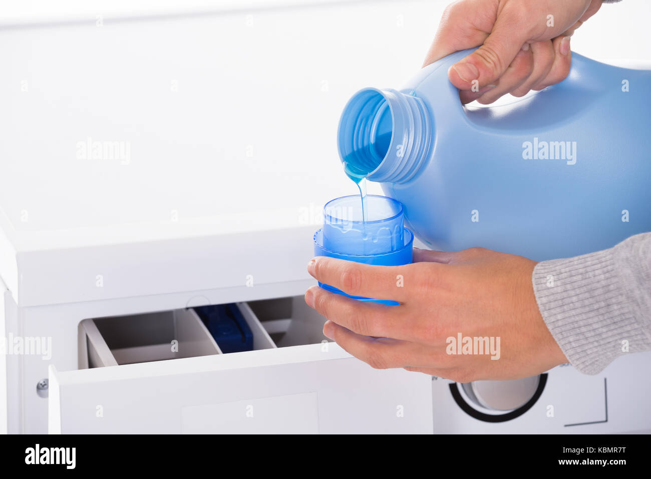 Cropped image of young woman's hand pouring detergent in lid with washing machine in background Stock Photo