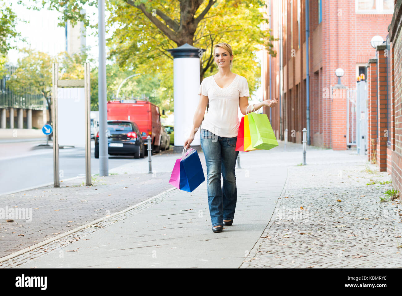 Full length portrait of happy woman carrying shopping bags on sidewalk Stock Photo