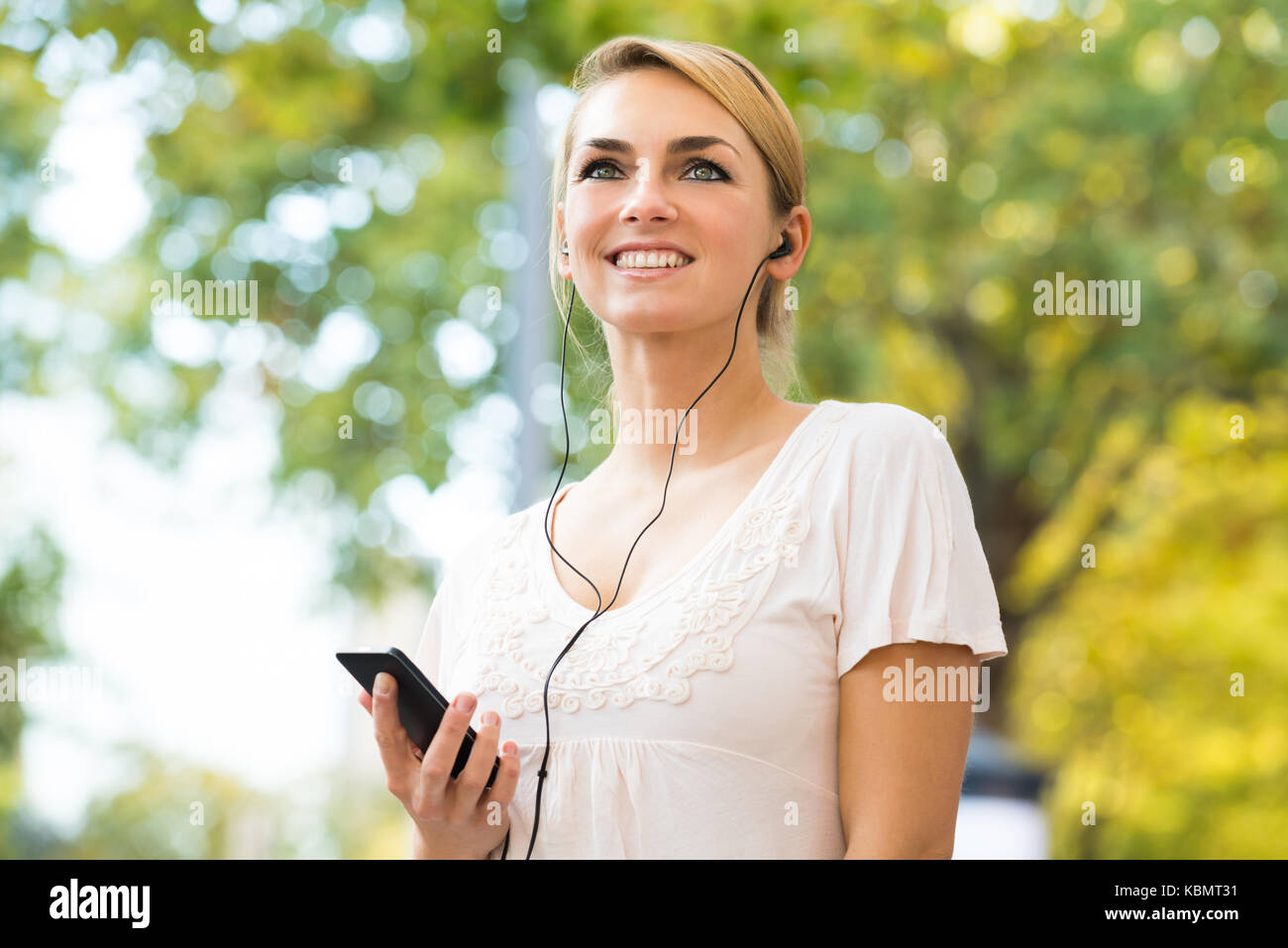 Smiling young woman listening to music through headphones using mobile phone Stock Photo