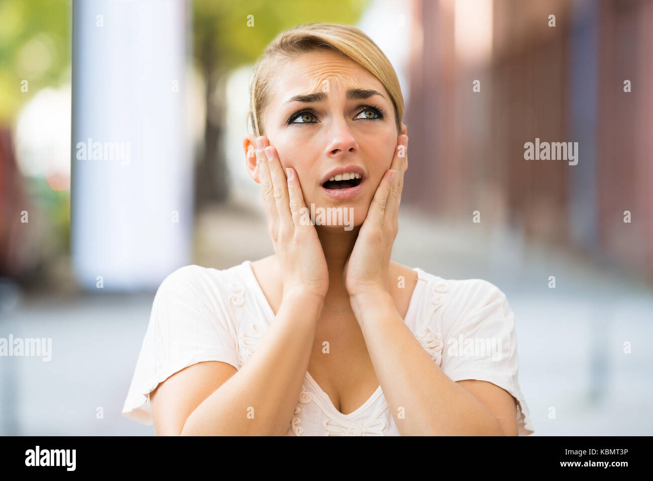 Shocked young woman with hands on face looking up Stock Photo
