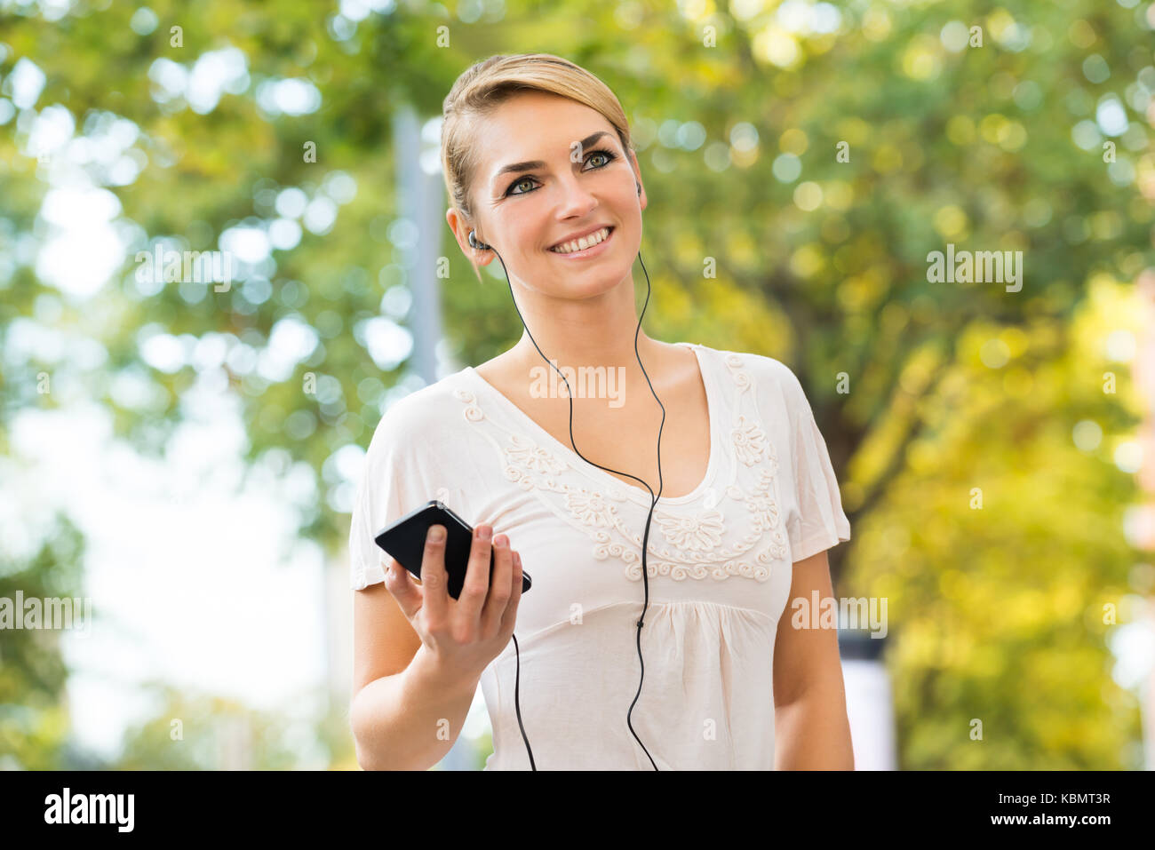 Smiling young woman listening to music through headphones using mobile phone Stock Photo