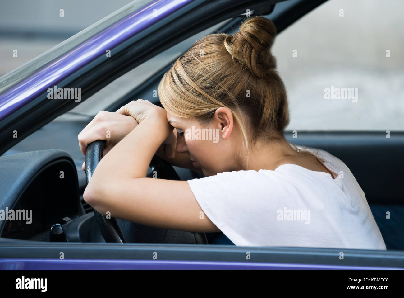 Side view of tired young woman leaning on steering wheel in car Stock Photo