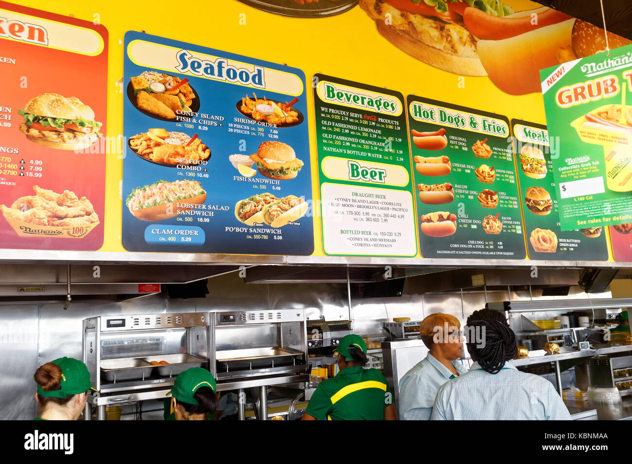 Worker's behind the counter at Nathan's Famous hot dog restaurant with the large menu board. Stock Photo