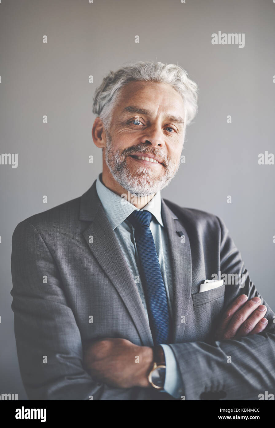 Portrait of a handsome mature businessman wearing a suit smiling confidently while standing alone in an office with his arms crossed Stock Photo
