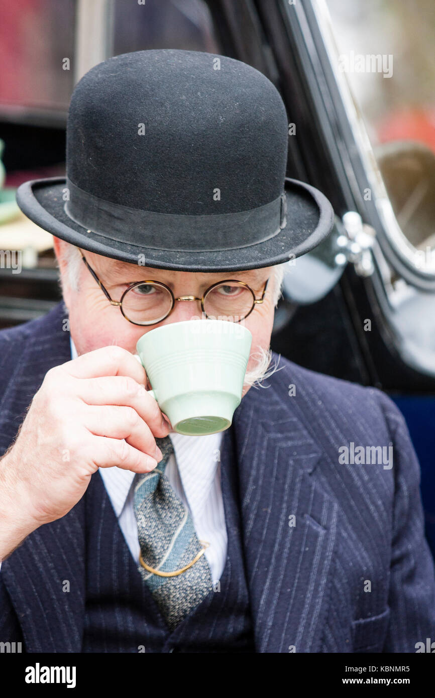 England, Chatham. Elderly man, grey moustache and glasses, wearing black bowler hat. Facing, eye-contact. Circa 1940s re-enactor. Drinking cup of tea. Stock Photo