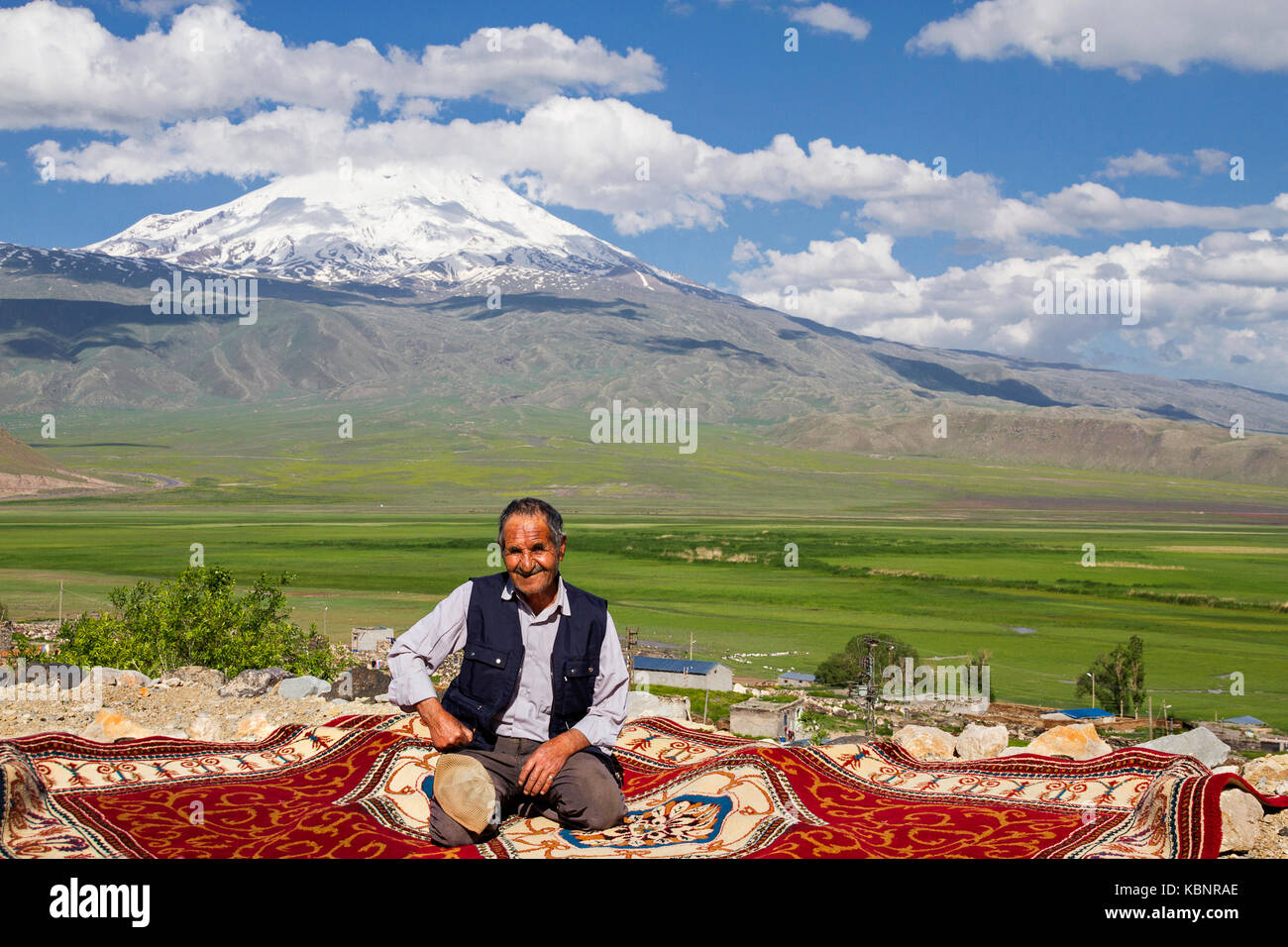 Kurdish man sitting on carpet, with the Mt Ararat in the background, in Dogubeyazit, Turkey. Stock Photo