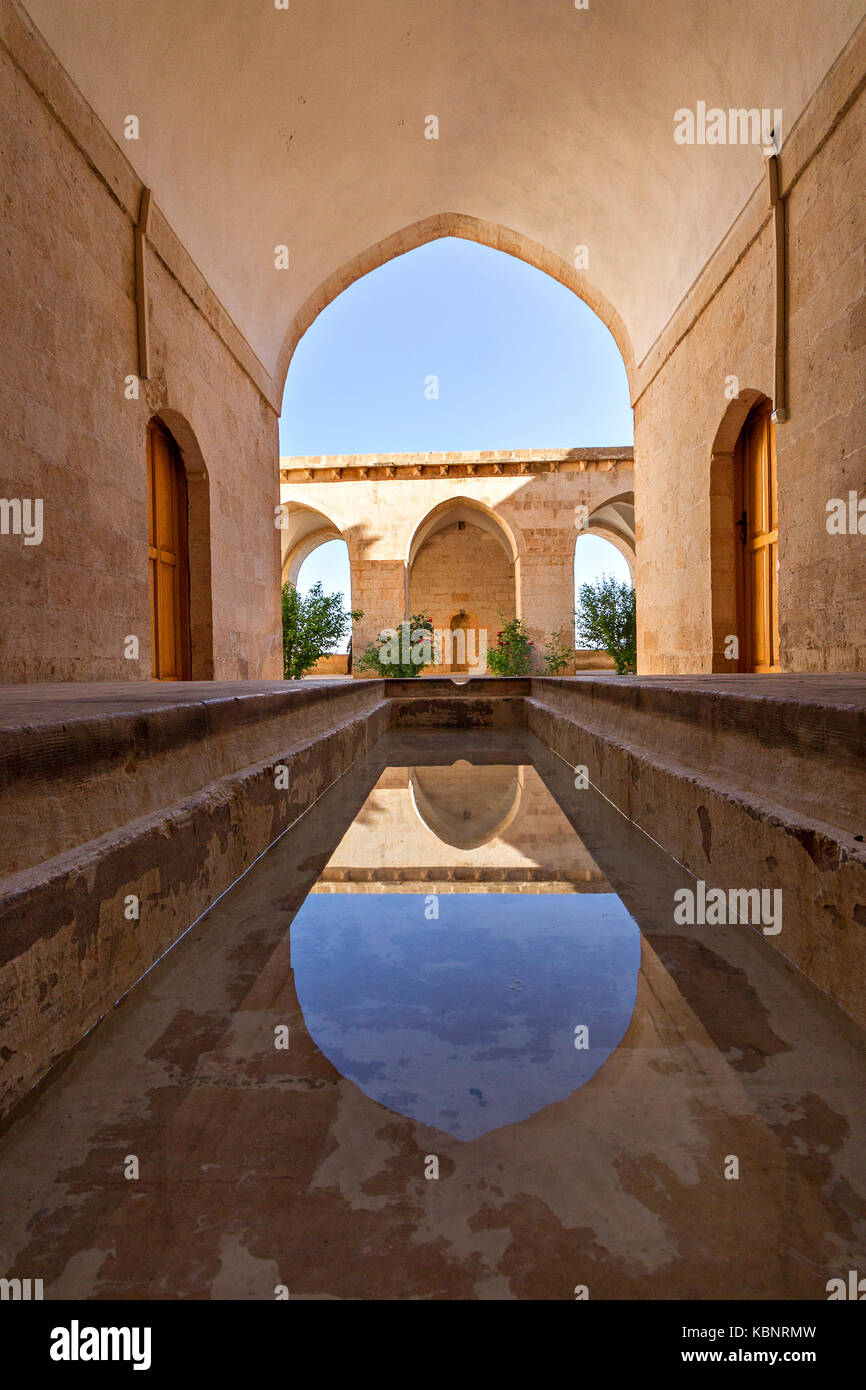 Ancient theological school known as Zinciriye Madrasah and reflection in its shallow pool in its courtyard, in Mardin, Turkey. Stock Photo