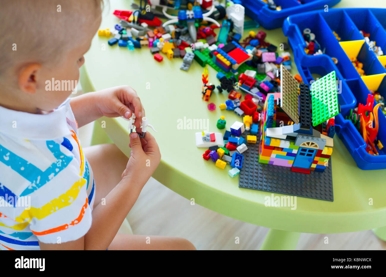 Little blond kid boy playing with lots of colorful plastic blocks ...
