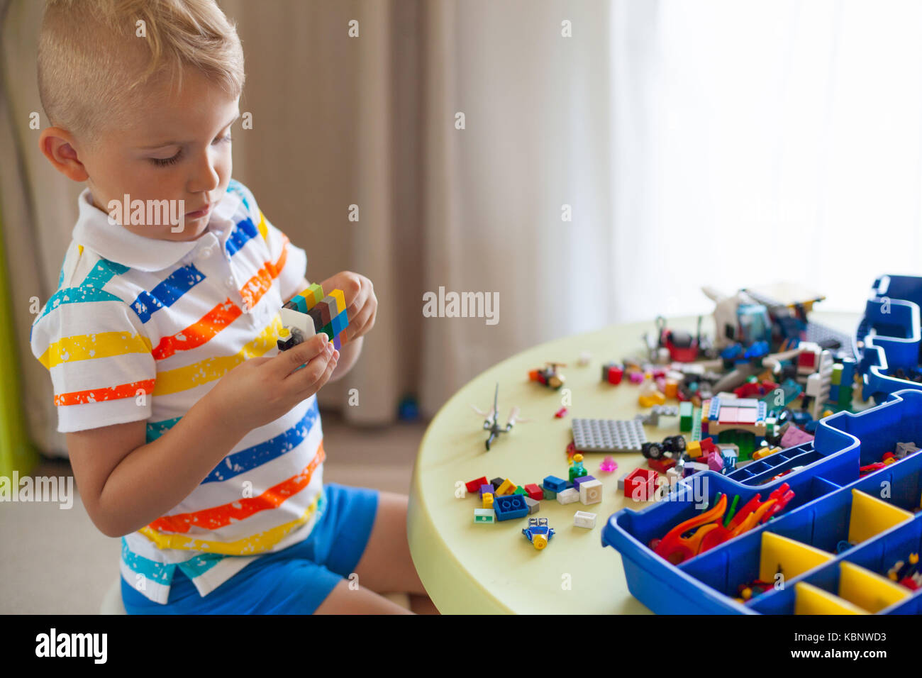 Little blond kid boy playing with lots of colorful plastic blocks ...