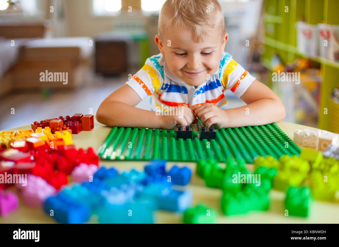 Little blond kid boy playing with lots of colorful plastic blocks ...