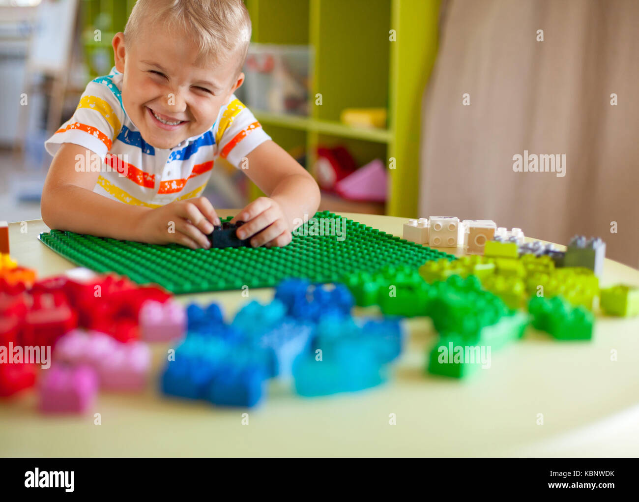Little blond kid boy playing with lots of colorful plastic blocks ...