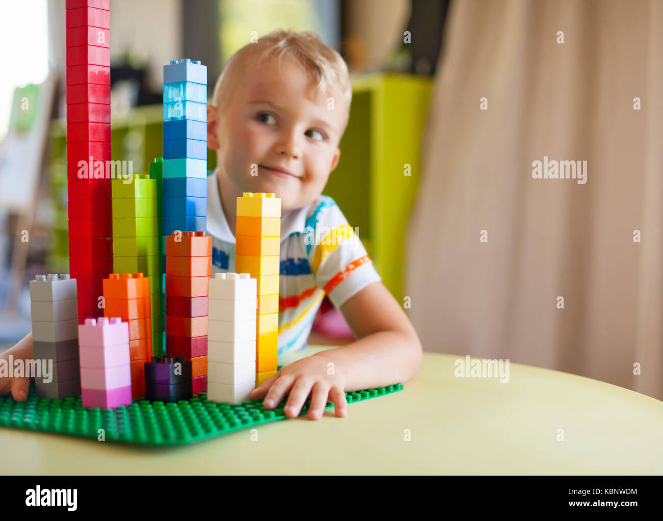 Little blond kid boy playing with lots of colorful plastic blocks ...