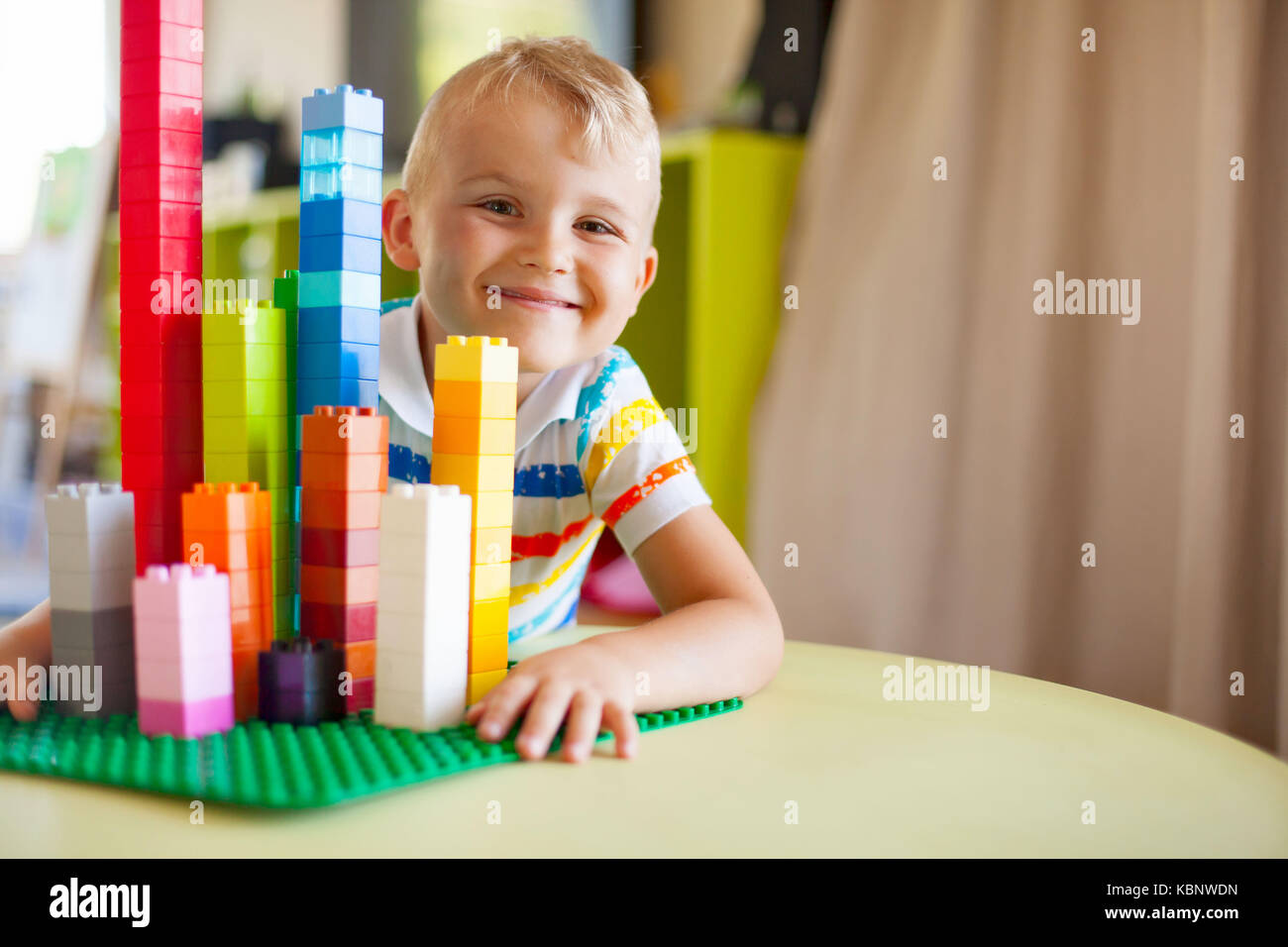 Little blond kid boy playing with lots of colorful plastic blocks ...