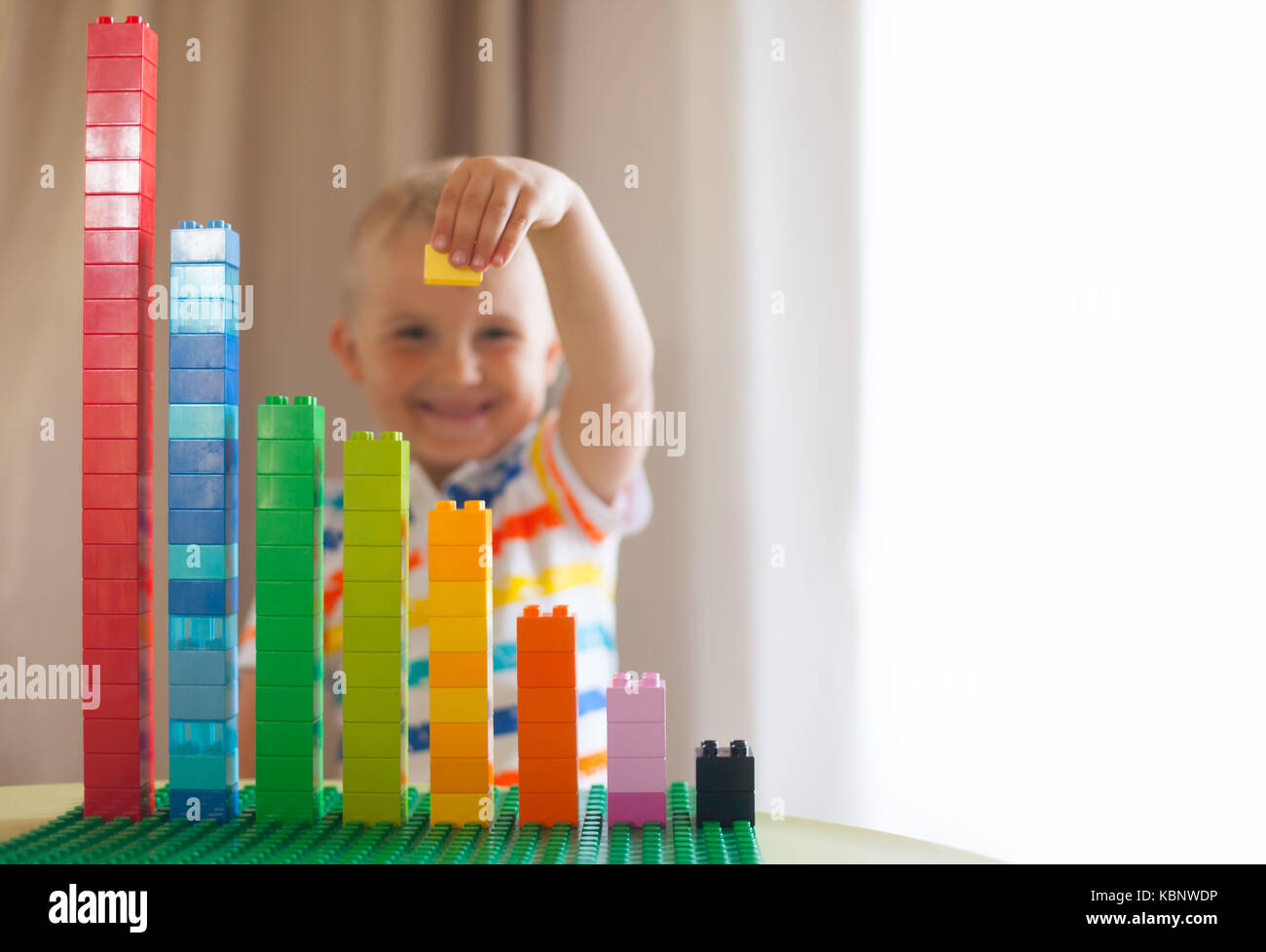 Little blond kid boy playing with lots of colorful plastic blocks ...