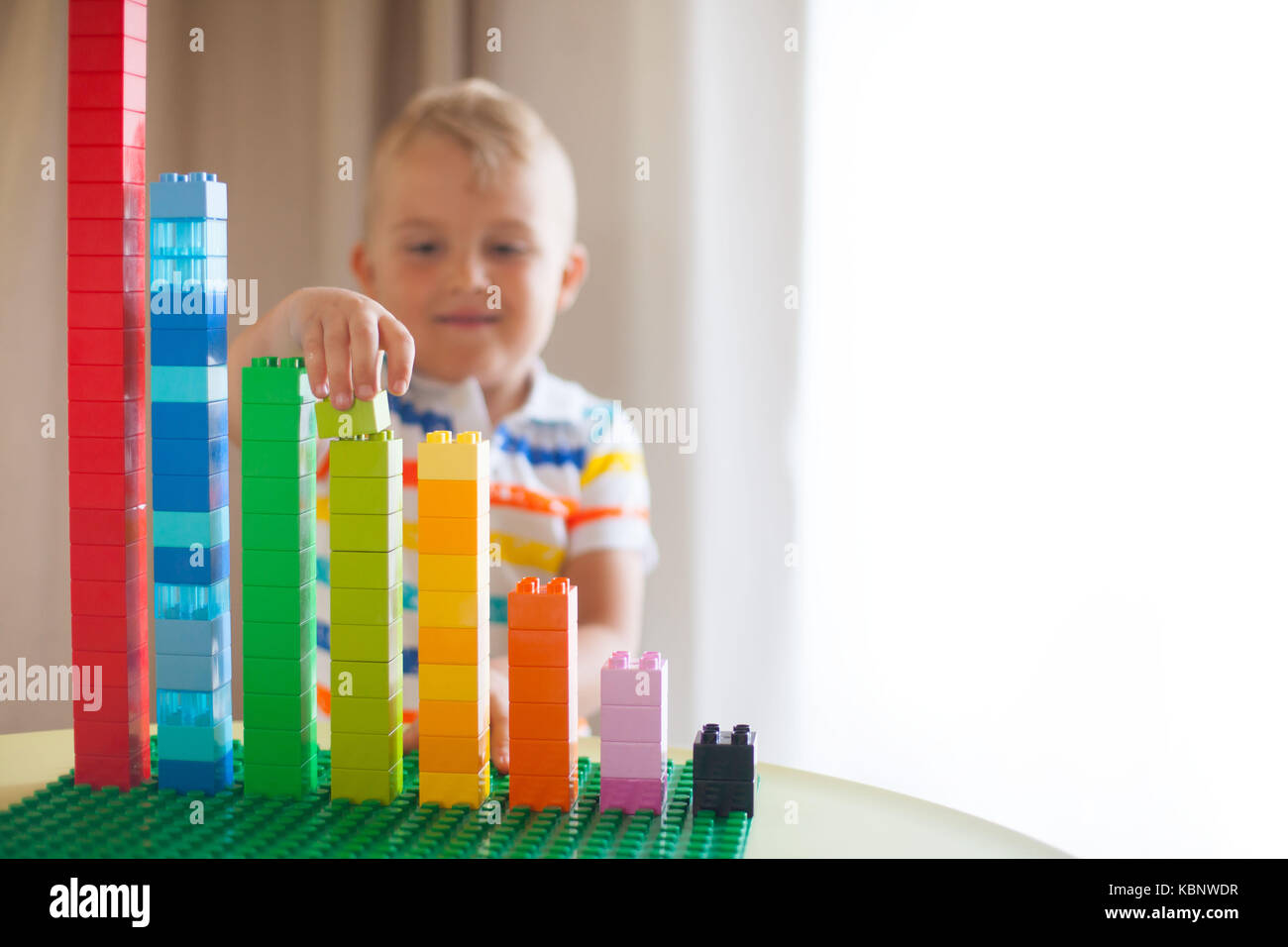 Little blond kid boy playing with lots of colorful plastic blocks ...