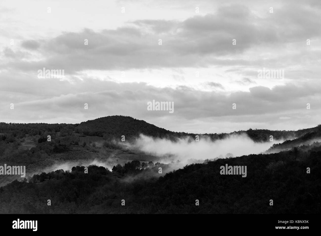 Mist in the middle of some hills, beneath an overcast sky Stock Photo