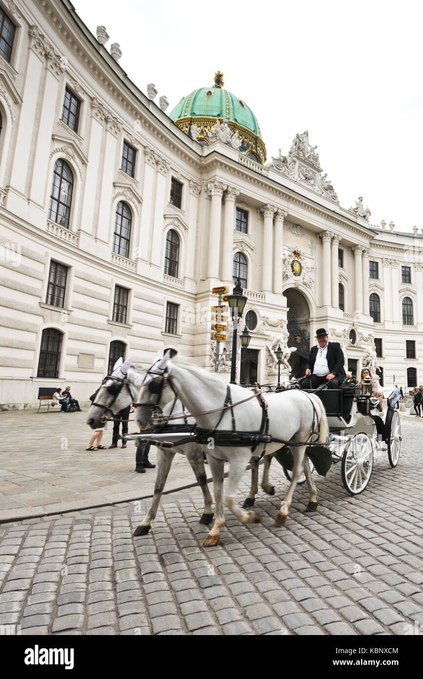 Famous horsedrawn carriage called fiaker passes by the Hofburg palace at Michaelerplatz in