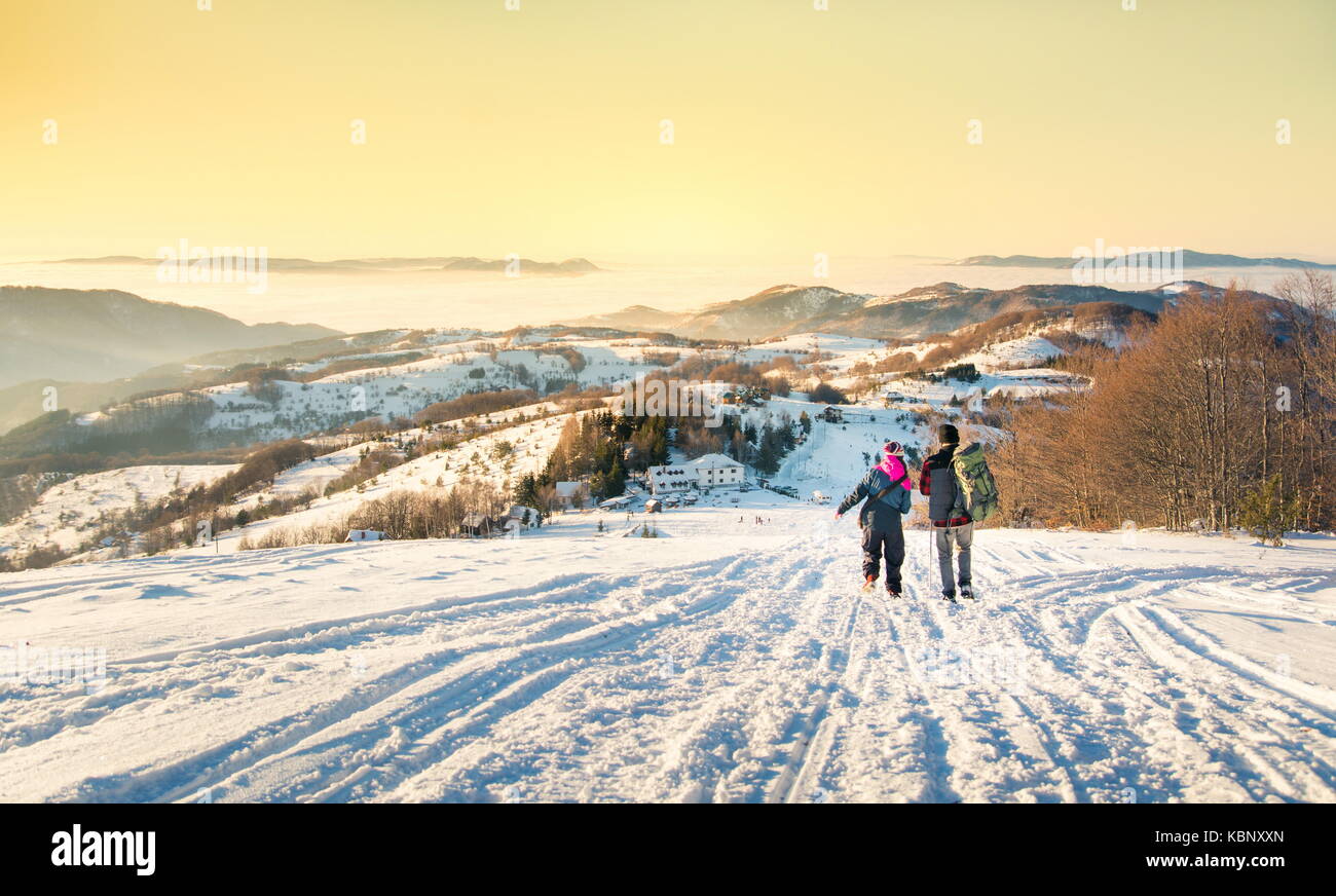 Couple walking down the snowy mountain at romantic sunset time Stock Photo