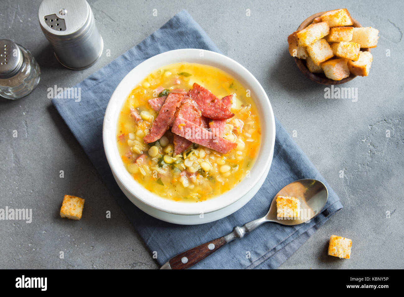 Split pea soup with smoked ham and croutons on grey background. Healthy