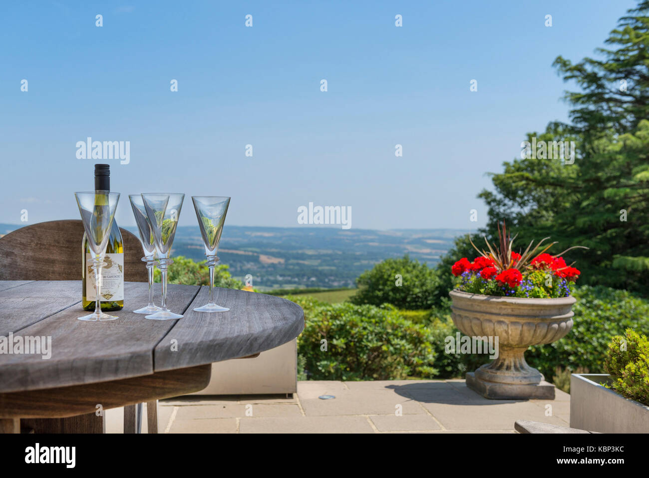 Wine bottle and glasses sit on a wooden garden table against a stunning view across Dartmoor in Devon on a sunny summer's day. Seafood Coast Stock Photo