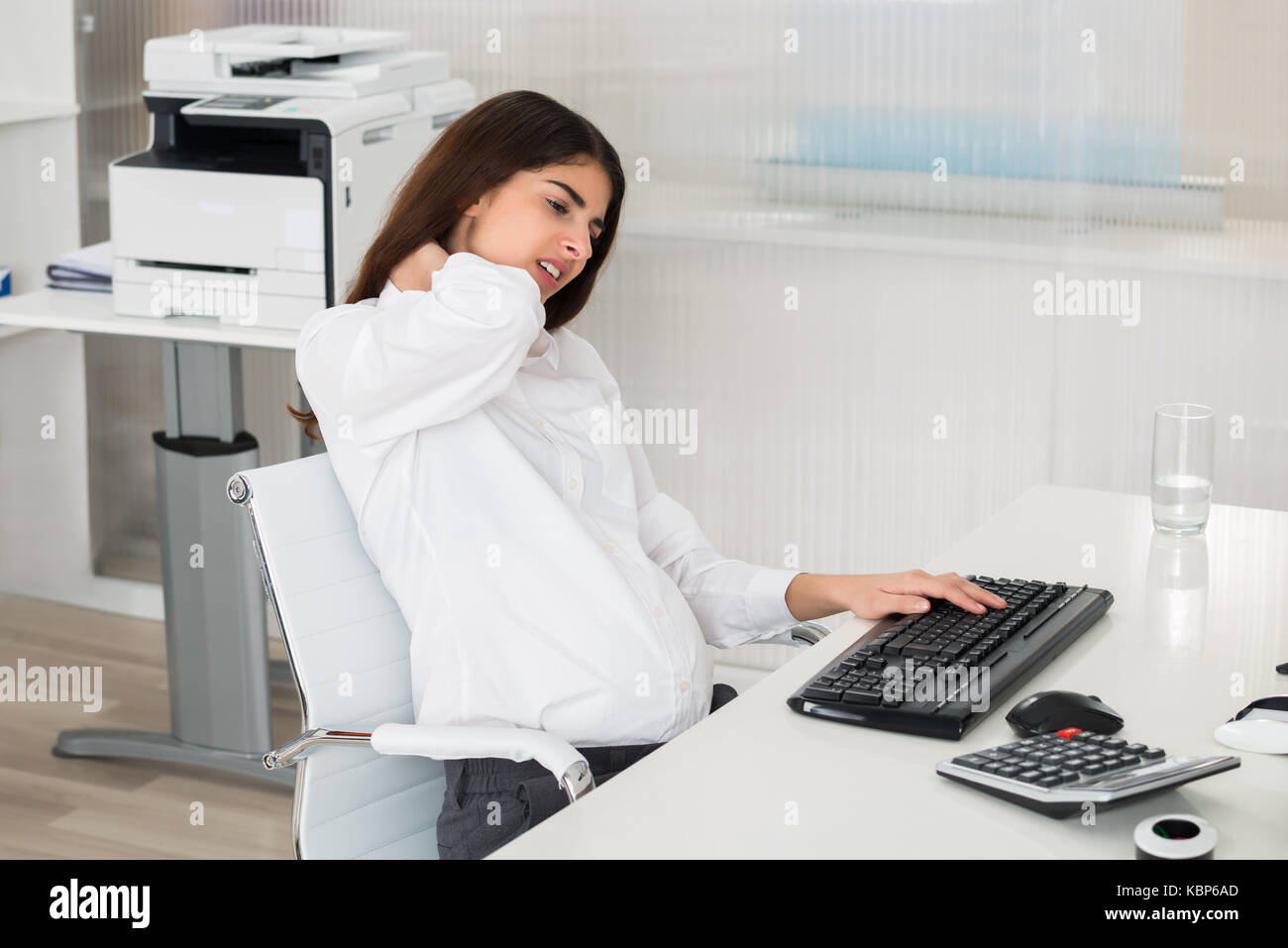 Young pregnant businesswoman suffering from neck pain while using