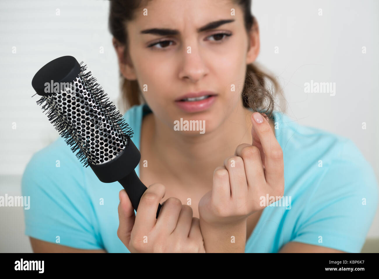 Shocked young woman holding comb while looking at hair loss Stock Photo