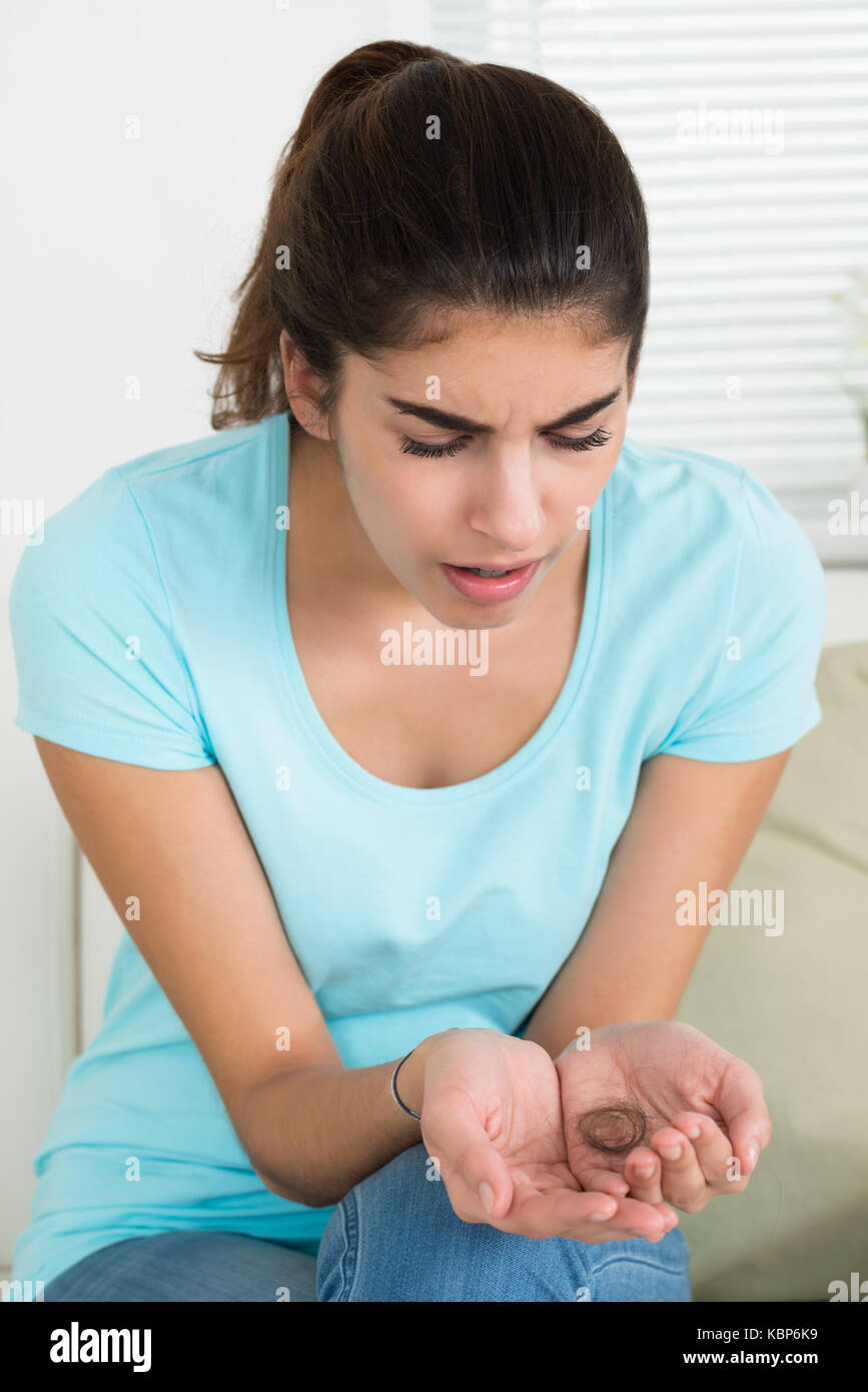 Surprised young woman looking at hair loss while sitting on sofa Stock Photo