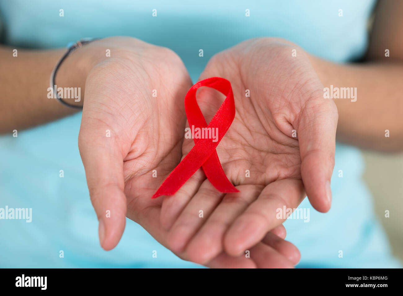 Closeup of woman holding AIDS awareness ribbon in palms at home Stock Photo