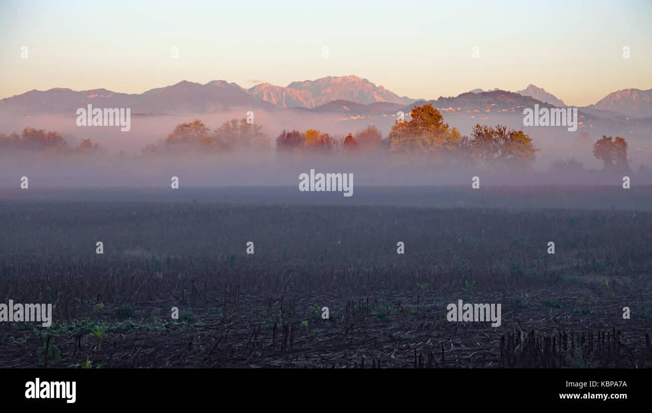 lots of fog in fields cultivated on a cold autumn day and mountains in the background Stock Photo