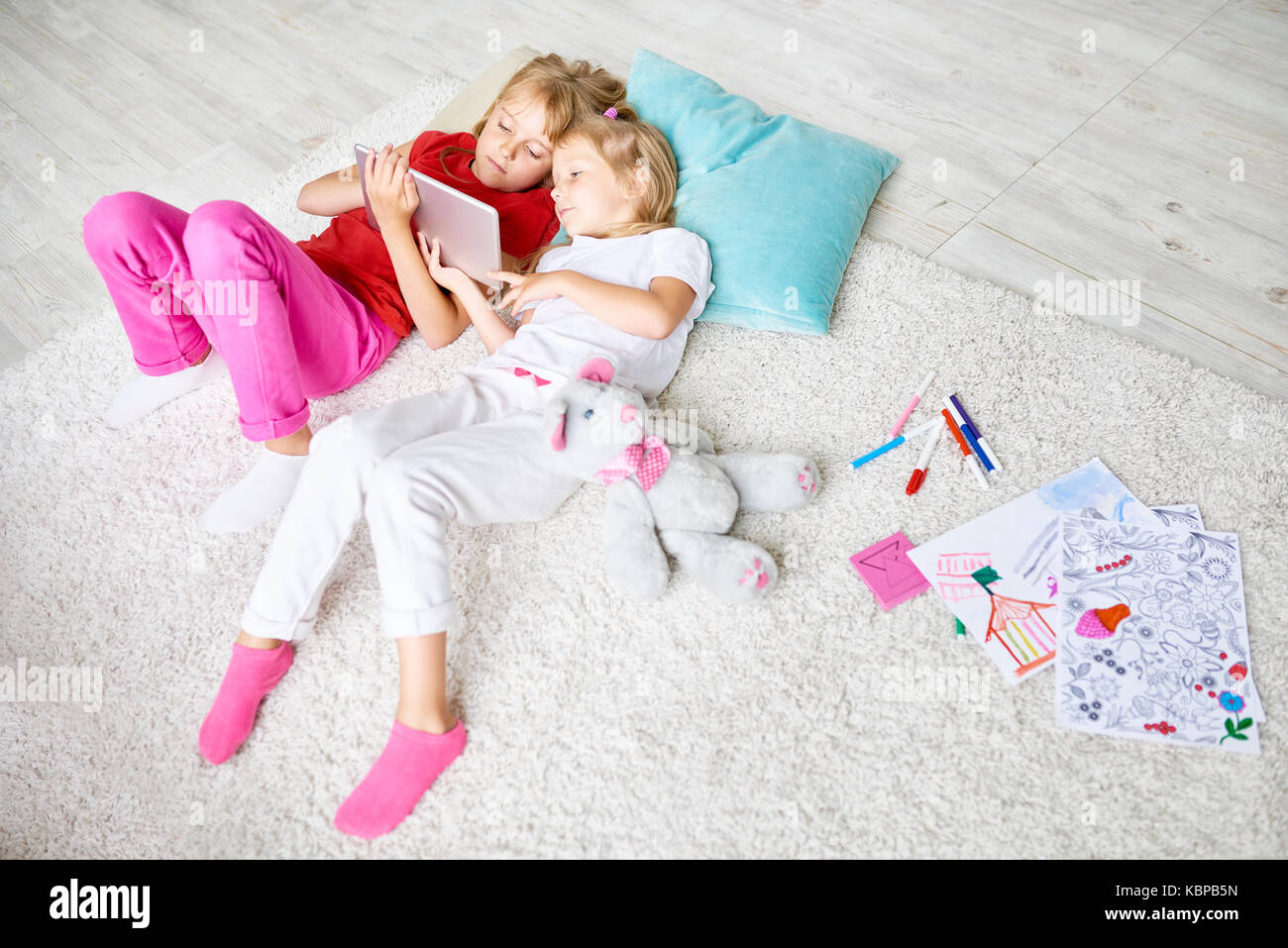 High angle portrait of two sisters using digital tablet lying on floor ...
