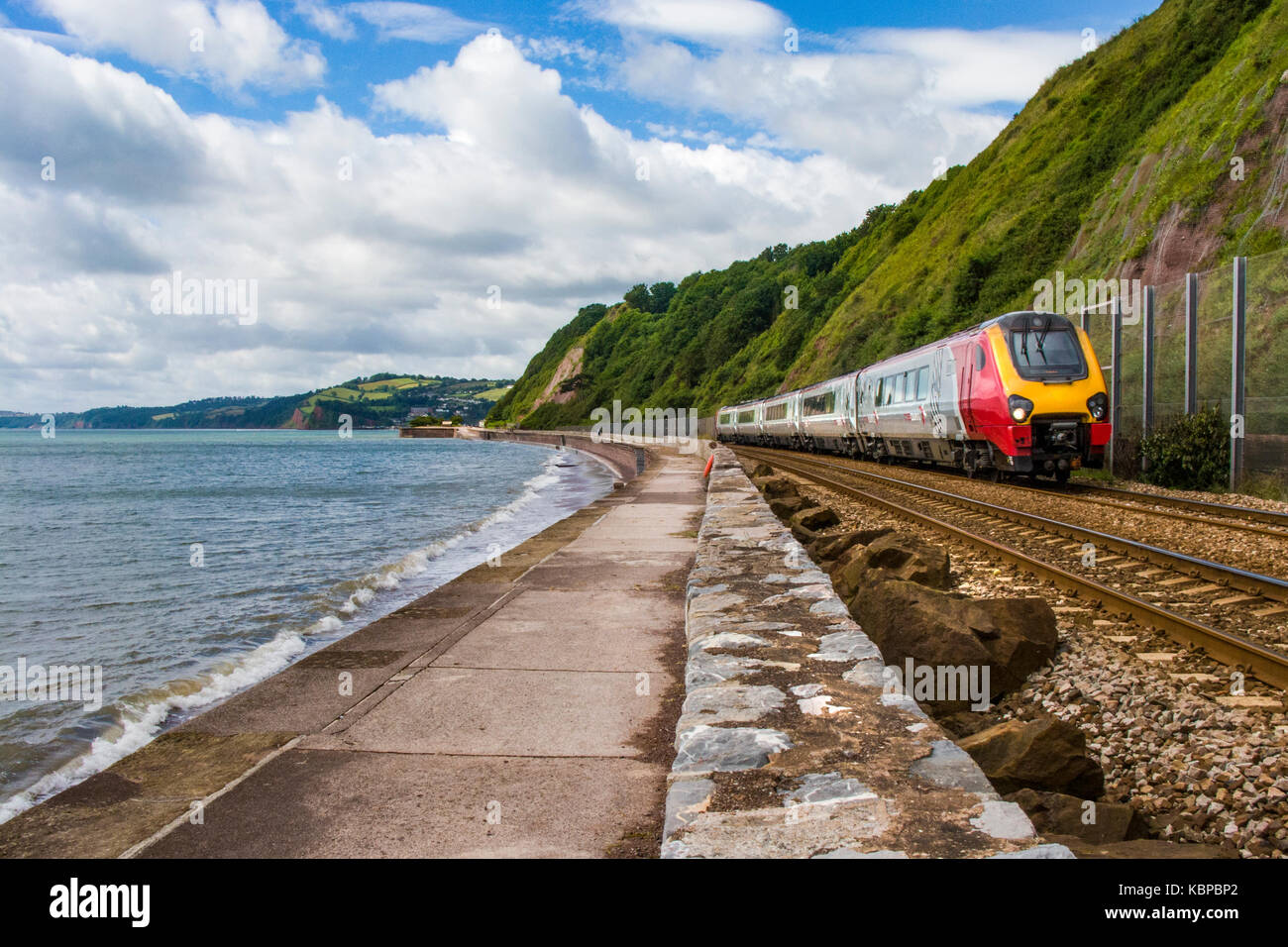 Train passing the south West Coast Path in Teignmouth, Devon UK alongside the beach. Vulnerable to flooding Stock Photo