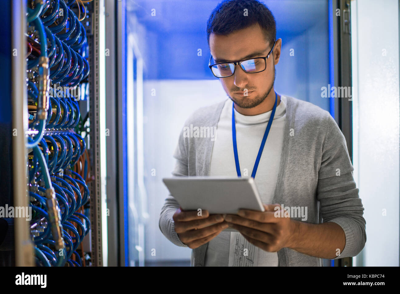 Portrait of young man using digital tablet standing by server cabinet ...