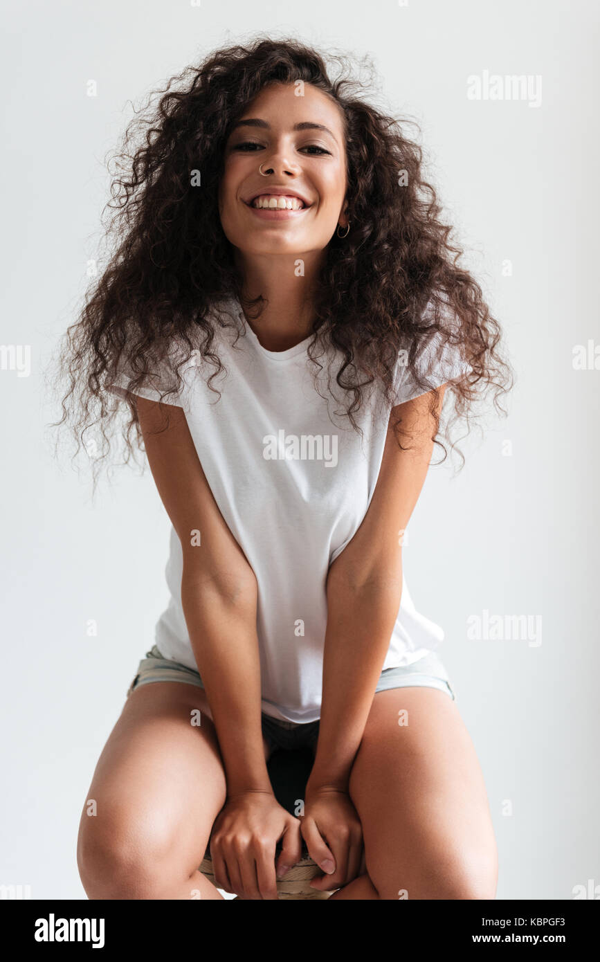 Happy cheerful girl with curly hair sitting on a chair and looking at ...