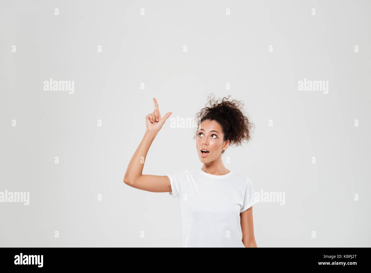 Surprised woman pointing up over gray background Stock Photo - Alamy