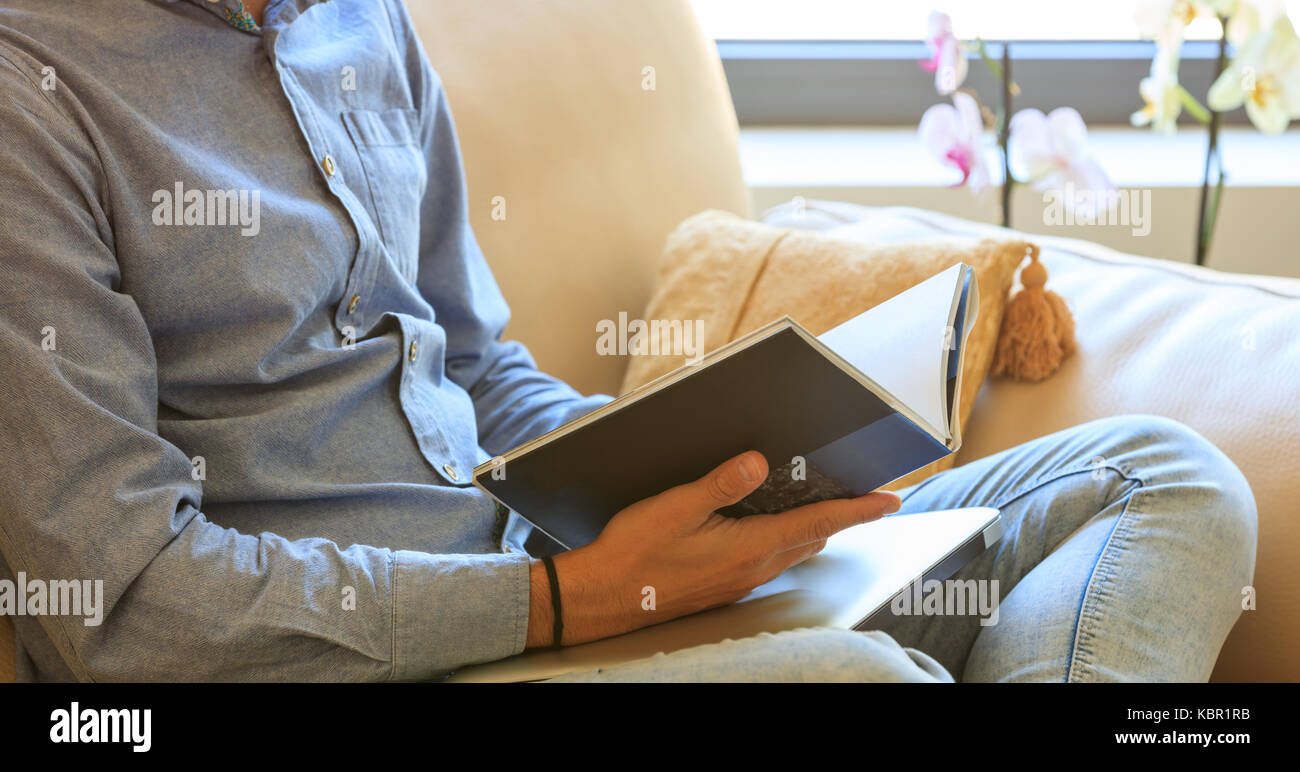 Young man reading a book sitting on a sofa at home Stock Photo