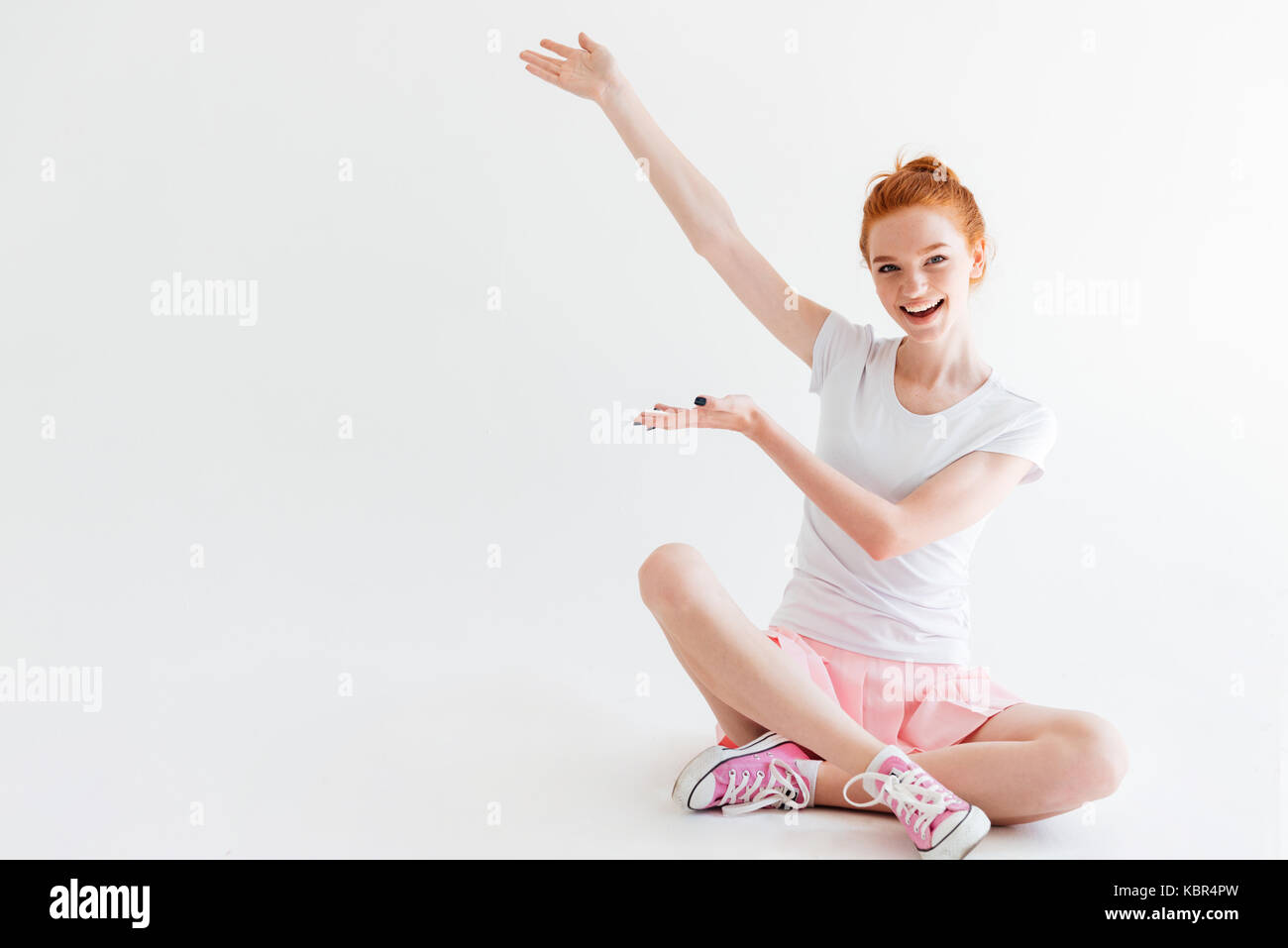 Happy ginger woman girl sitting on the floor and showing something over ...