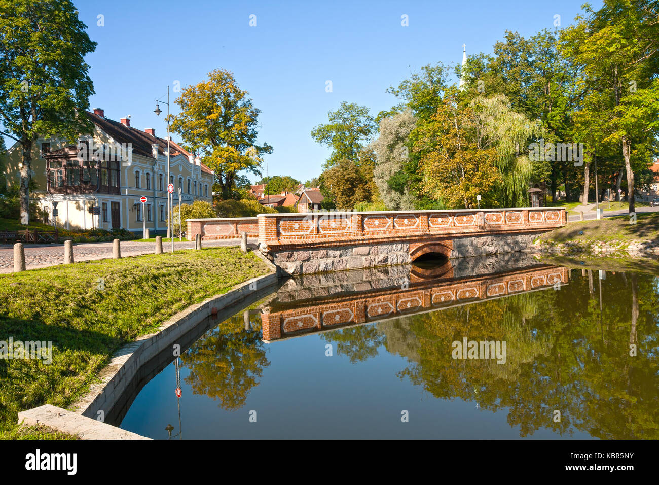 Stone bridge, reflected in the pond, Kuldiga, Latvia. On the building an inscription on Lettish language 'Kuldiga's court' Stock Photo