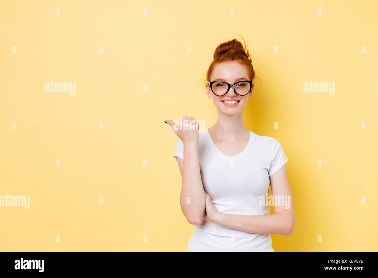 Smiling ginger girl in eyeglasses pointing away and looking at the ...
