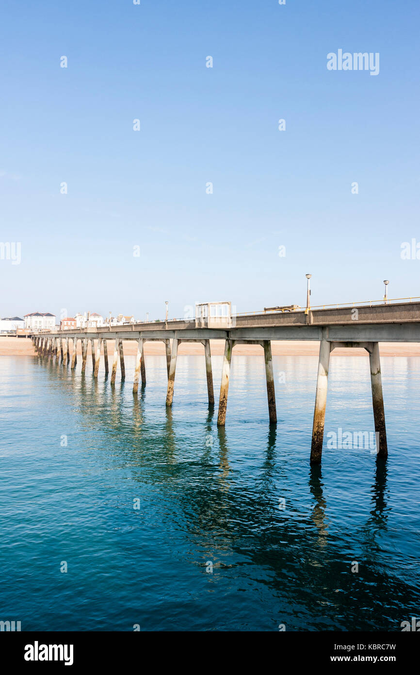 England, Deal pier. View of length of pier and beach with part of the town. Clear blue sky, daytime, bright sunshine. Very calm sea. Stock Photo