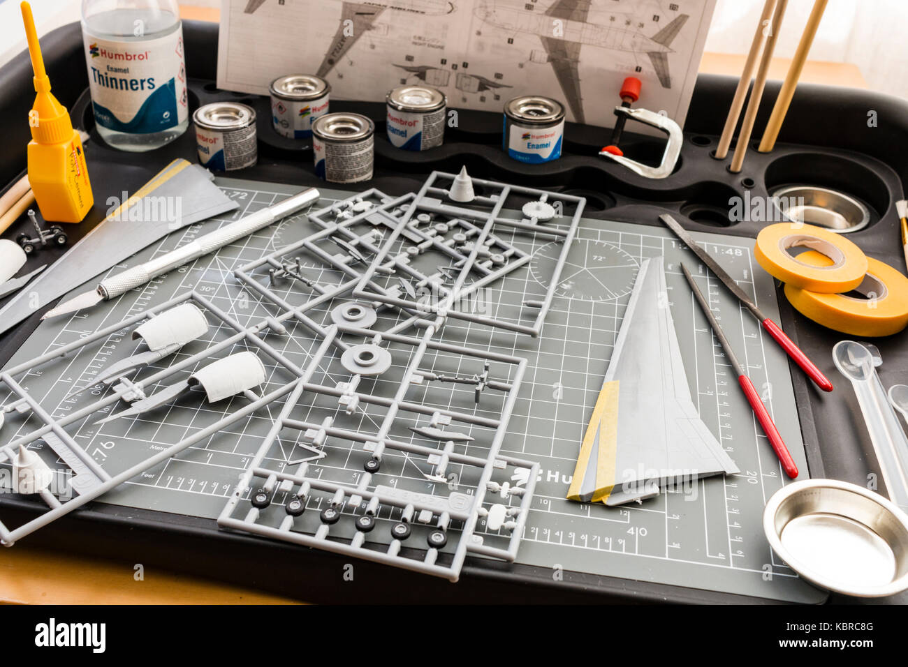 England. Modelling station with cutting mat, paint pots, tools, maskign tape. Spur of airplane parts, and plane wing partly masked for painting. Stock Photo