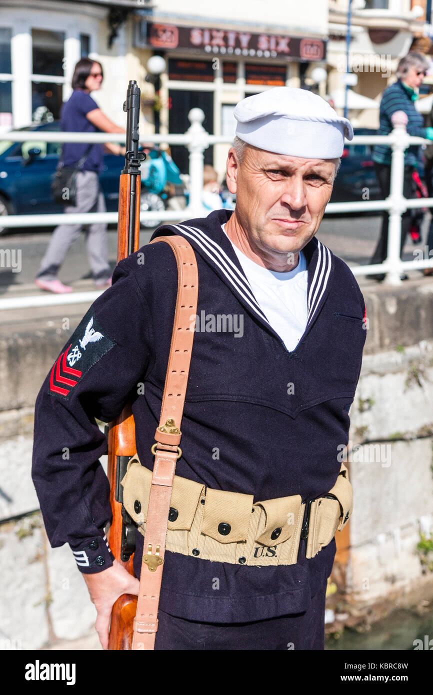 England. Re-enactment. World war two US Navy sailor, sergeant, on standing guard duty, eye-contact, smiling. Rifle slung over shoulder. Stock Photo