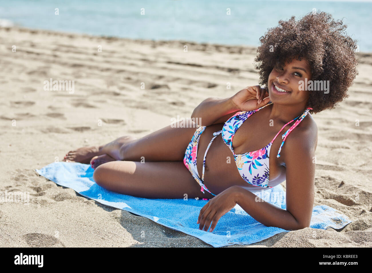 Portrait of happy afro american woman lying on beach with hand on neck Stock Photo
