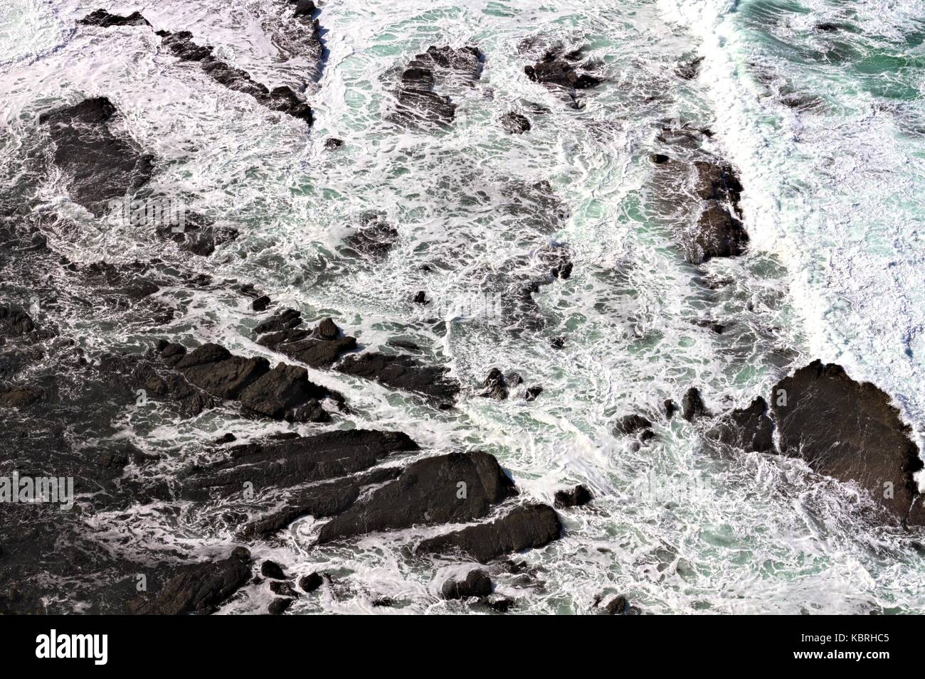 View from above of surf breaking over rocks. Stock Photo