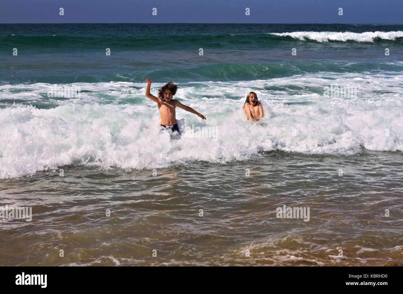 Two boys happily jumping in the cold waves of Marengo Beach in early spring, Australia. Stock Photo