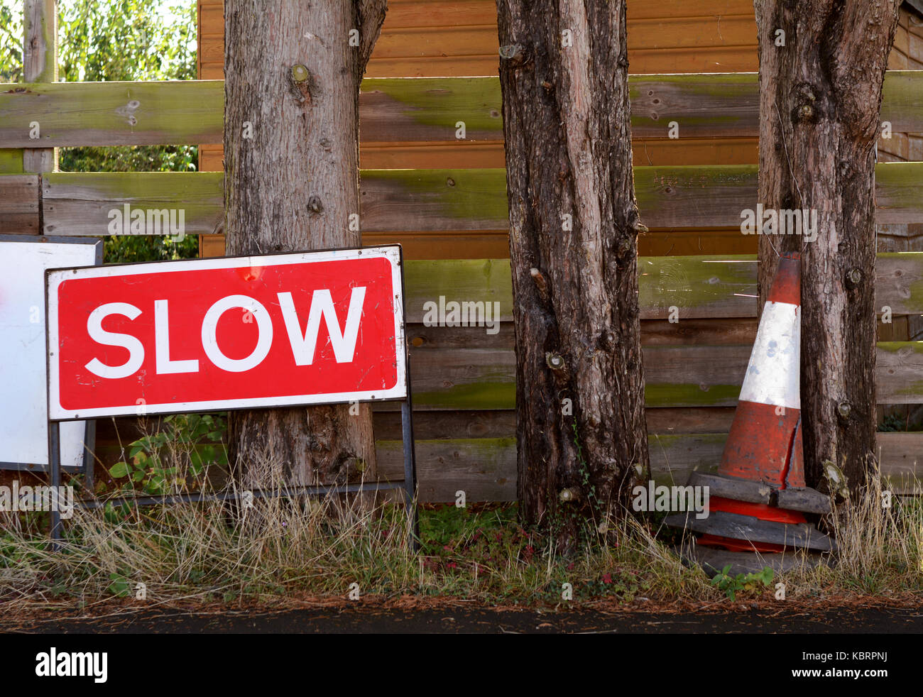 SLOW traffic sign with broken orange and white traffic cones, stored on the verge against tree trunks Stock Photo