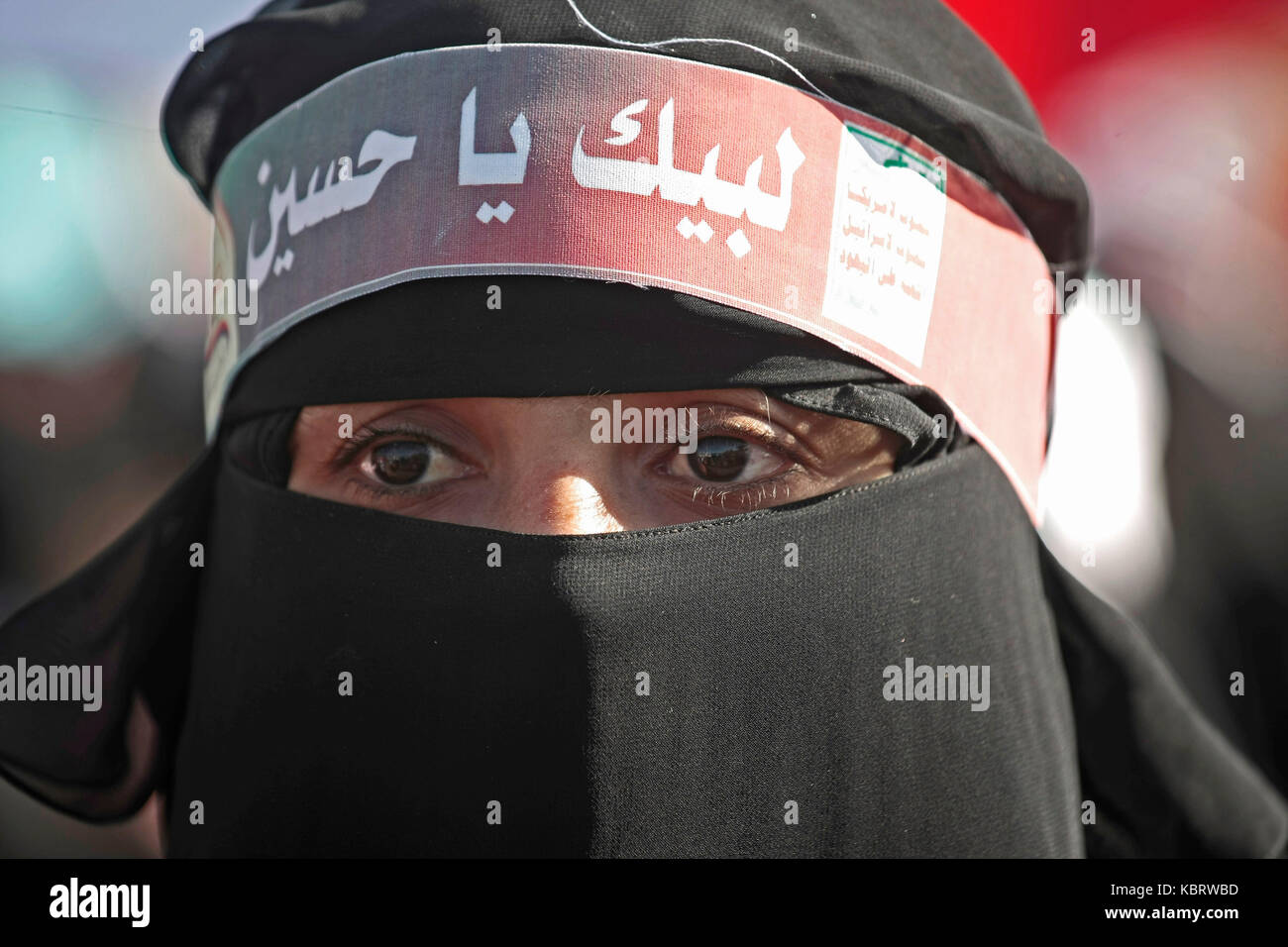 A Yemeni woman wears a head band with Arabic reading,