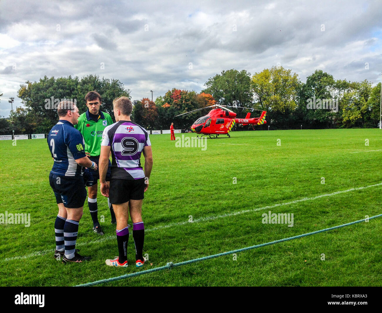 Woodford Green, London, UK. 30th September 2017. Referee confers with team captains as London’s  Air Ambulance helicopter G-LNDN lands at Woodford Rugby Football Club's Highams ground in Woodford Green in response to a report of a spectator suffering a heart attack. The Woodford v Chelmsford match was suspended for 40 minutes whilst paramedics attended to the casualty who was able to leave by road.  Woodford went on to win the match. The Air Ambulance is supported by London Freemasons.  Credit: Mark Dunn/ Alamy Live News Stock Photo