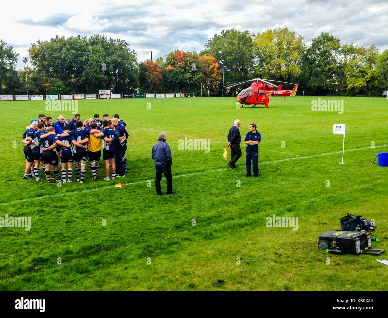Woodford Green, London, UK. 30th September 2017. Players confer as London’s  Air Ambulance helicopter G-LNDN lands at Woodford Rugby Football Club's Highams ground in Woodford Green in response to a report of a spectator suffering a heart attack. The Woodford v Chelmsford match was suspended for 40 minutes whilst paramedics attended to the casualty who was able to leave by road.  Woodford went on to win the match. The Air Ambulance is supported by London Freemasons.  Credit: Mark Dunn/ Alamy Live News Stock Photo